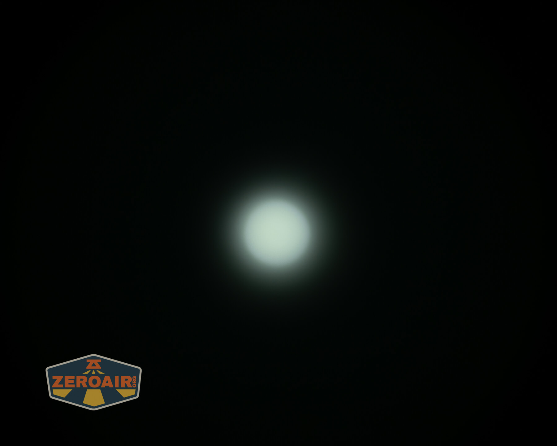 A bright, circular white light is centered against a dark background. The light appears slightly diffused with a subtle glow. A logo in the bottom left corner displays the text ZEROAIR.