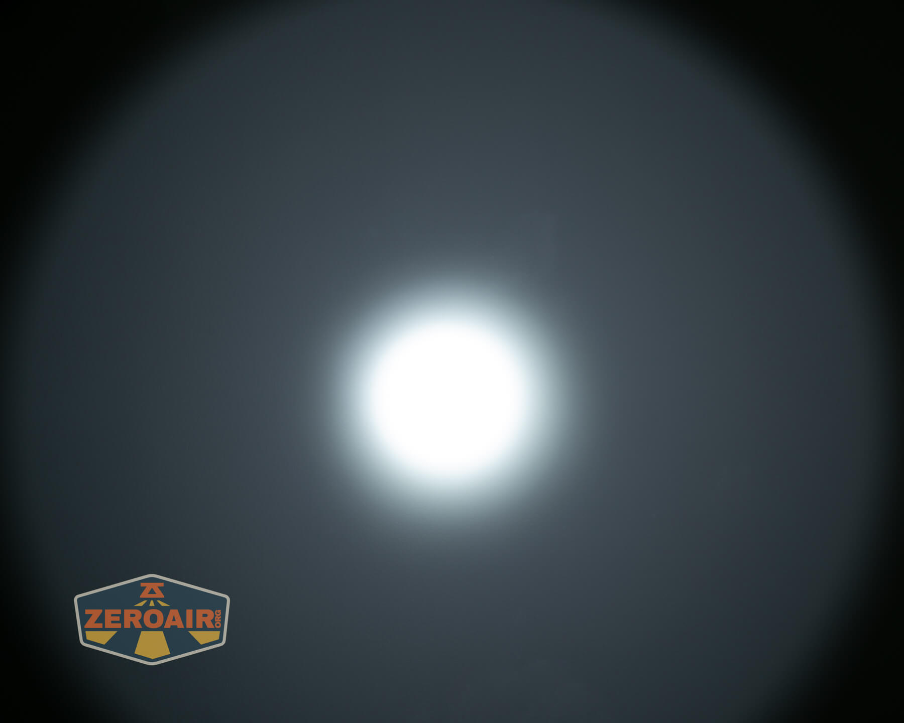 A bright white circular light appears in the center of a dark background, with a soft halo effect around it. A ZEROAIR logo is visible in the lower left corner.