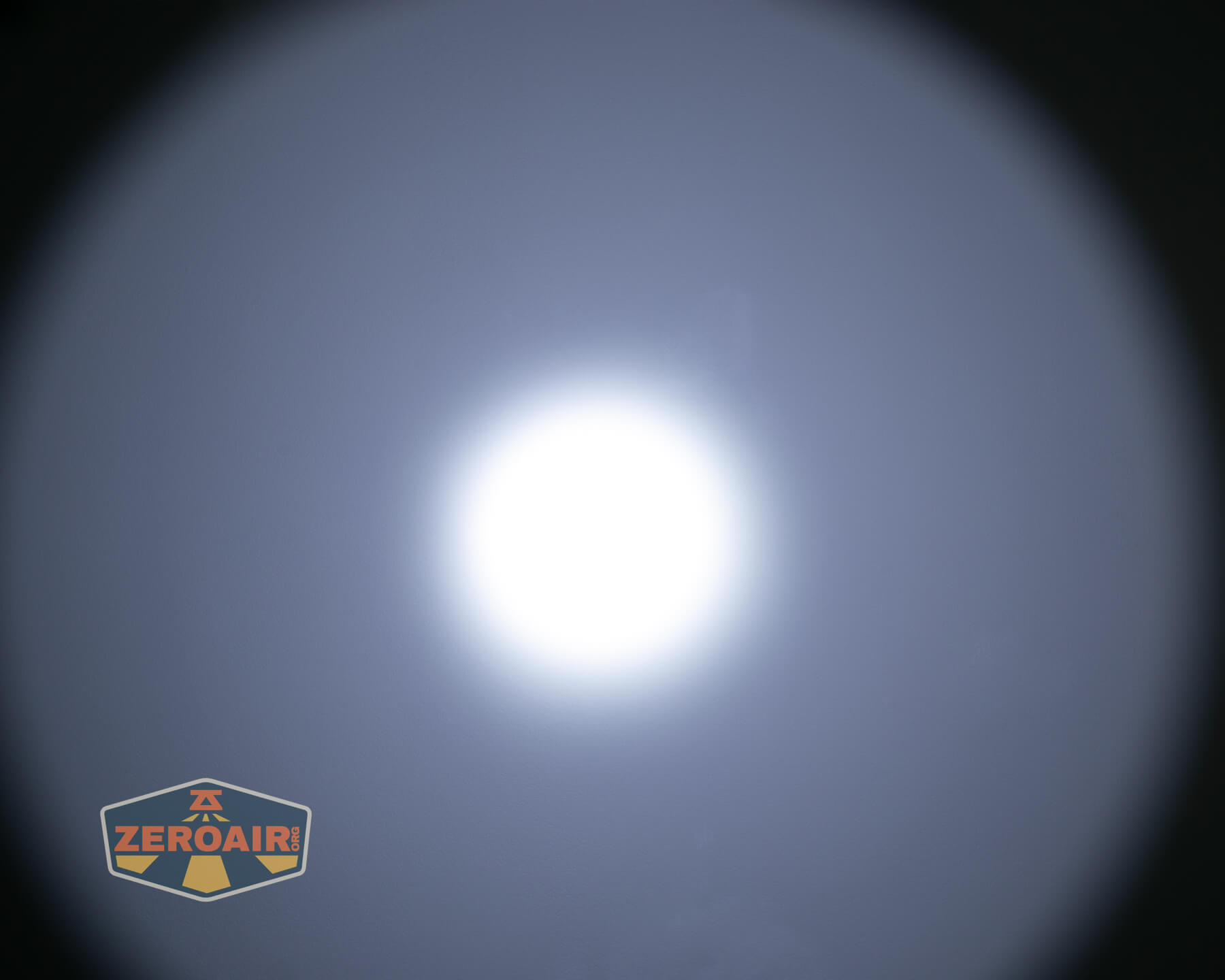 A bright circular white light beam shines in the center of a dark background. The ZeroAir logo appears in the bottom left corner of the image.