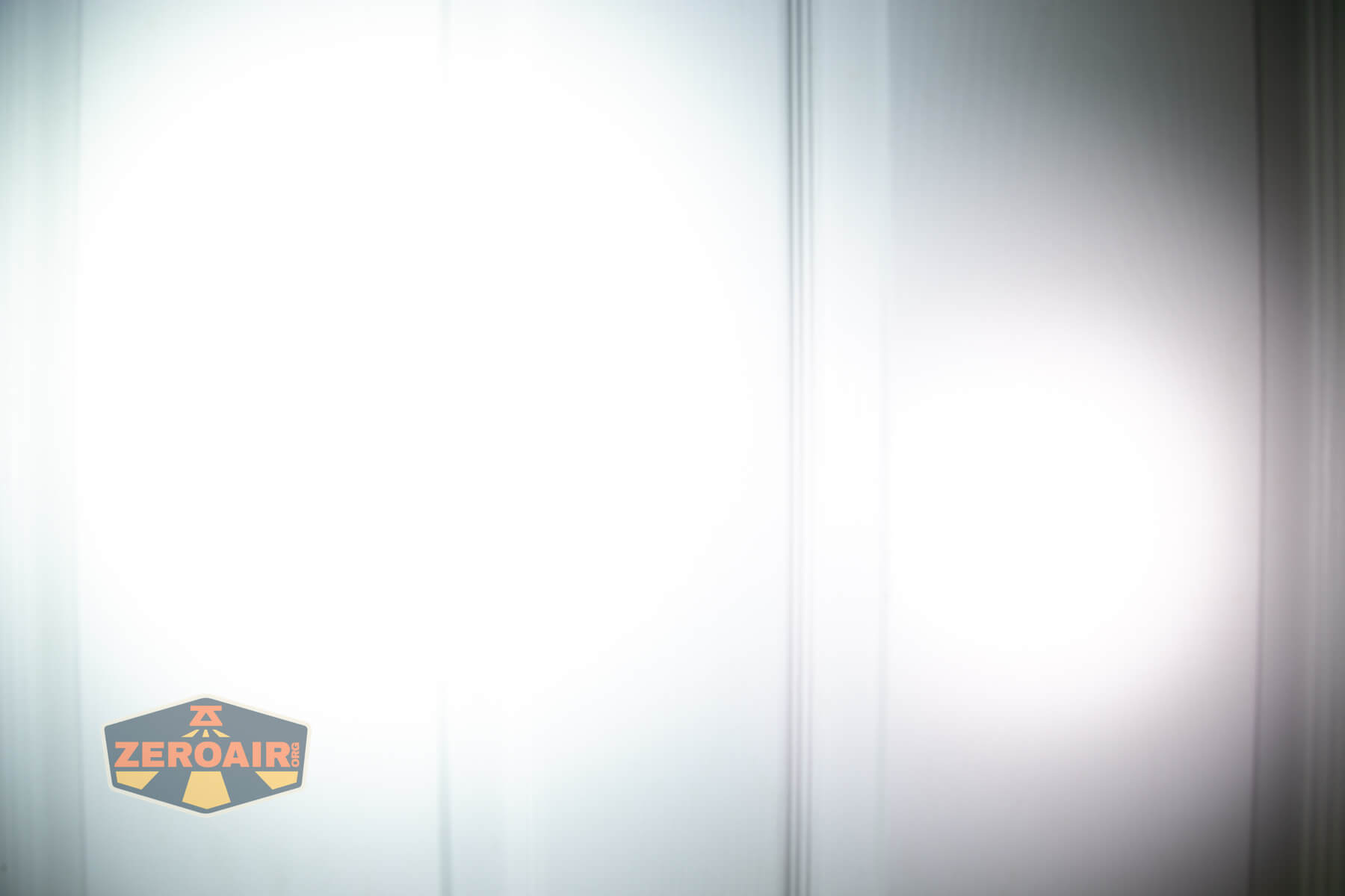 A bright white circular light beam is projected onto a light-colored paneled door. The ZeroAir logo is visible in the bottom left corner of the image.