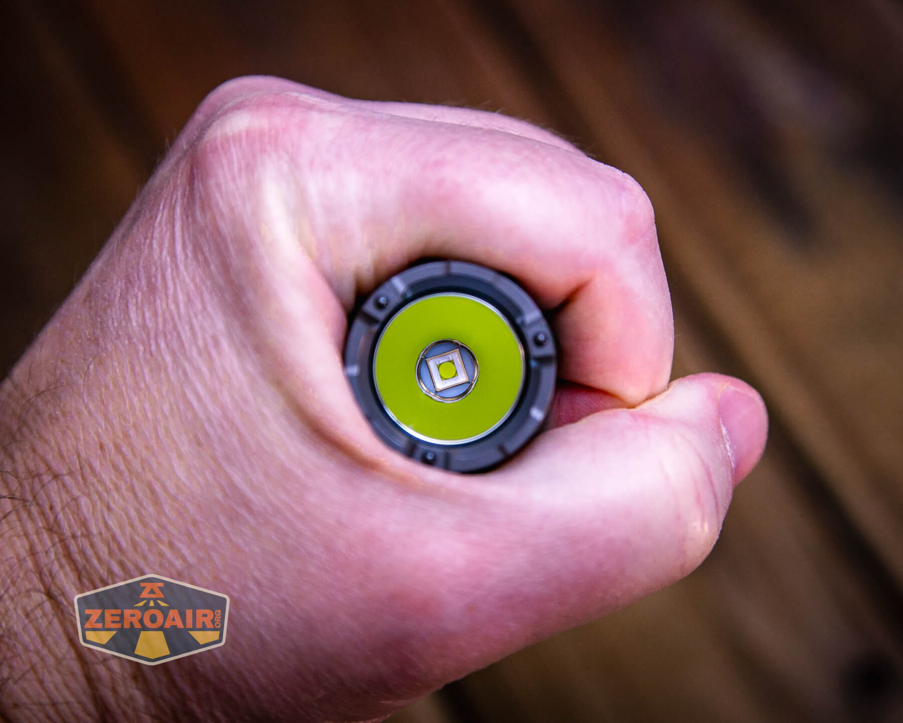 A hand holding a flashlight pointed directly at the camera, showing the light’s LED bulb. The flashlight brand logo ZeroAir appears in the bottom left corner.