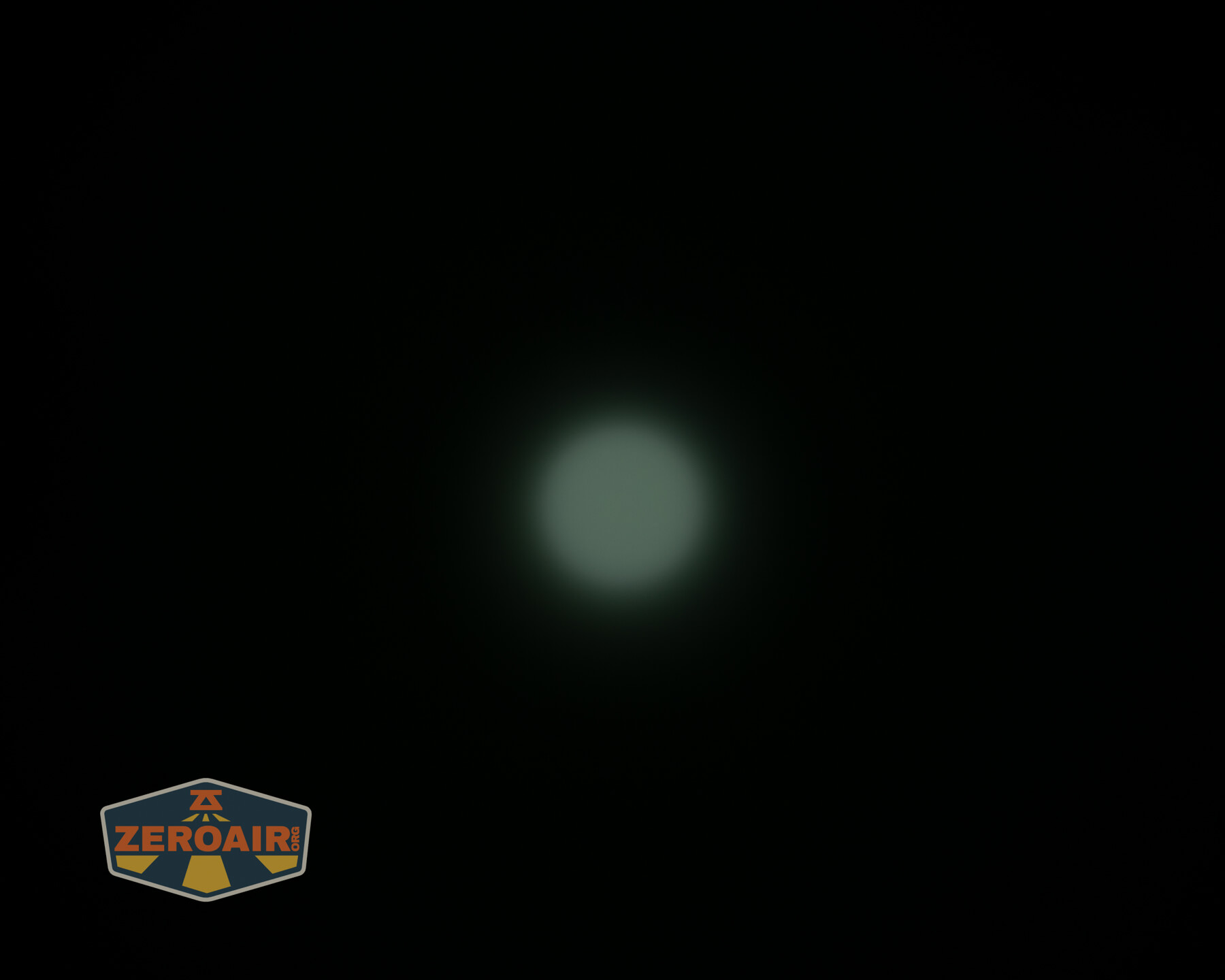 A bright circular light source with a faint glow is centered against a completely black background. A logo with the text ZEROAIR appears in the bottom left corner.