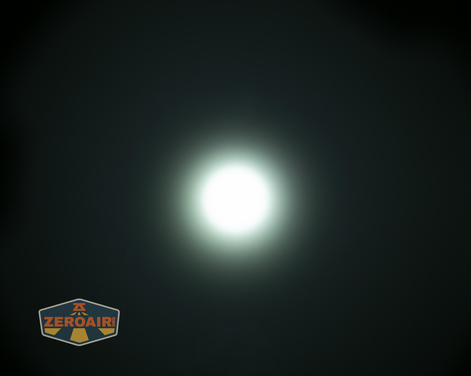A bright white circular light source glows at the center of a dark background, with a faint halo around it. A small shield-shaped logo with the text ZeroAir appears in the lower-left corner.