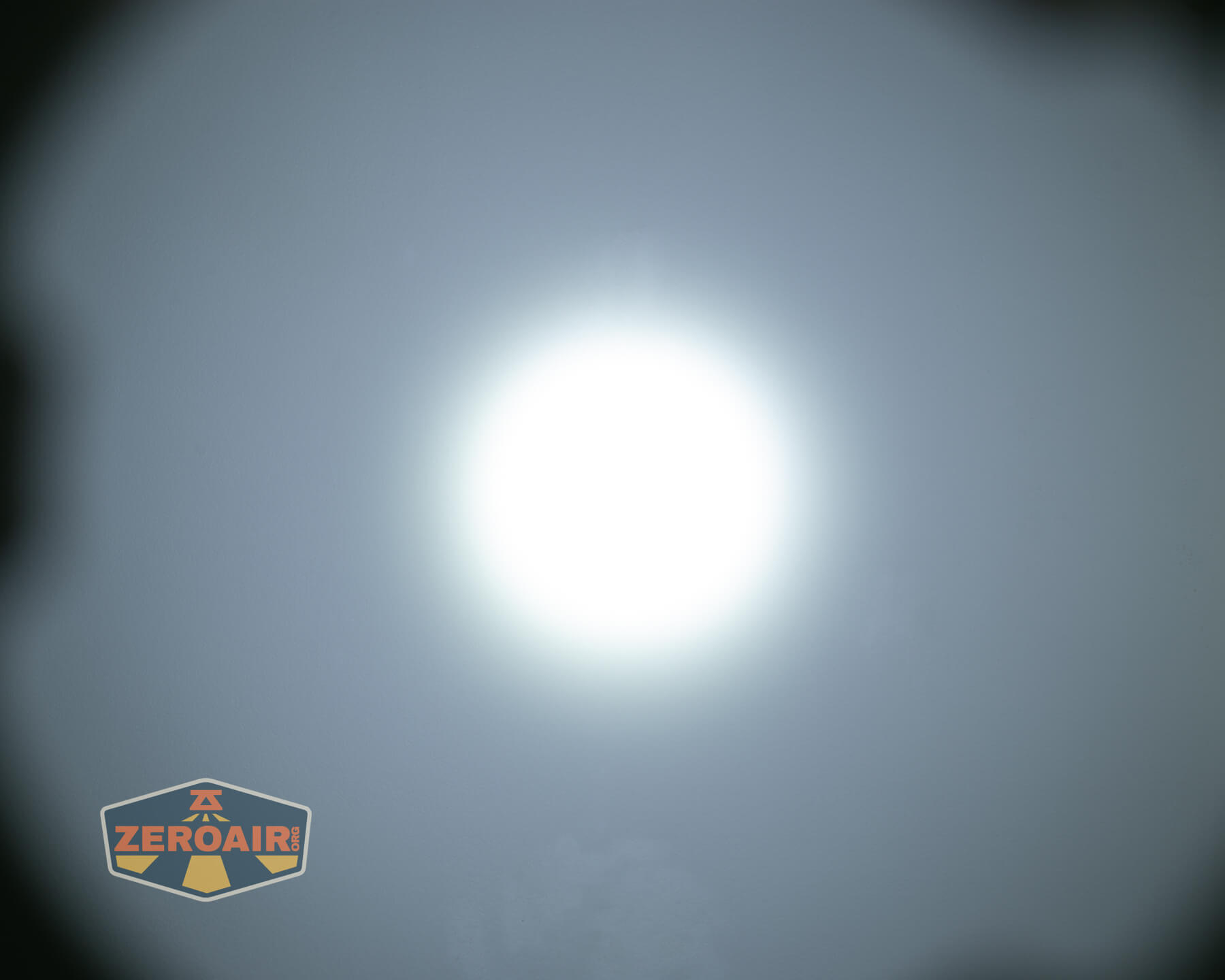 A circular, bright white light is centered against a gray background with slightly darker corners. A ZEROAIR logo appears in the bottom left corner.