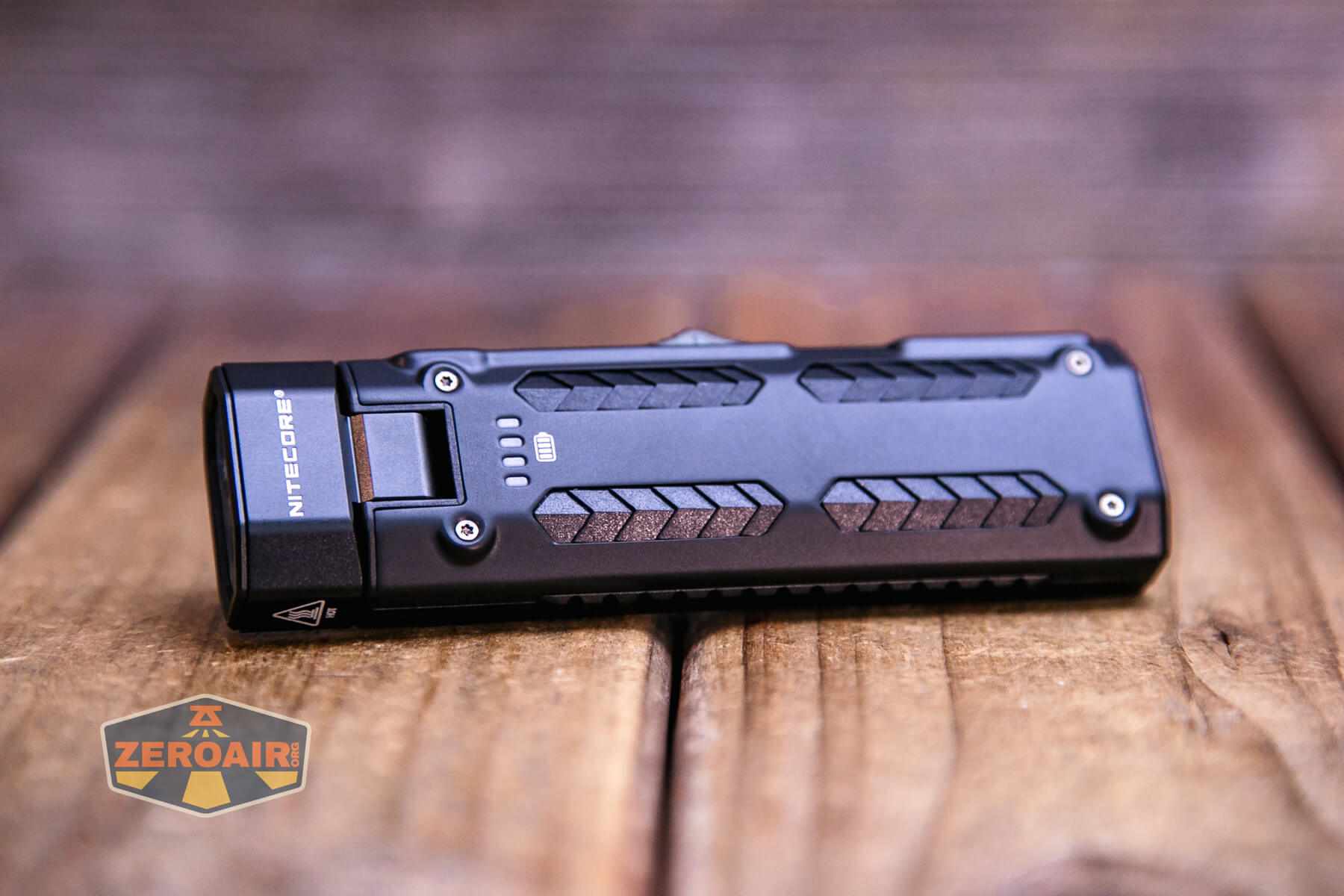 A black Nitecore flashlight with a rectangular body and textured grip patterns lies on a wooden surface. The logo ZEROAIR is visible in the lower left corner of the image.