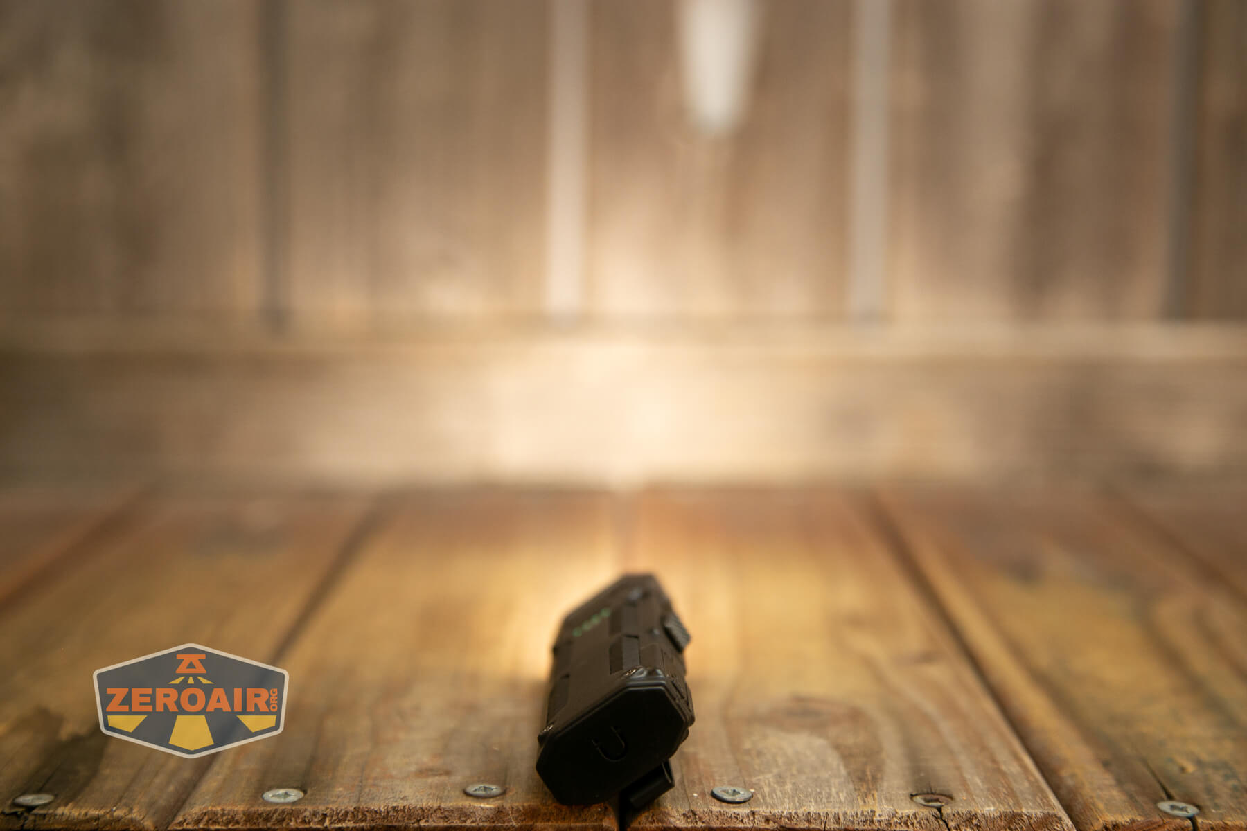 A black flashlight is placed on a wooden surface in the foreground with a blurred wooden background. A logo reading ZEROAIR is visible in the bottom left corner.