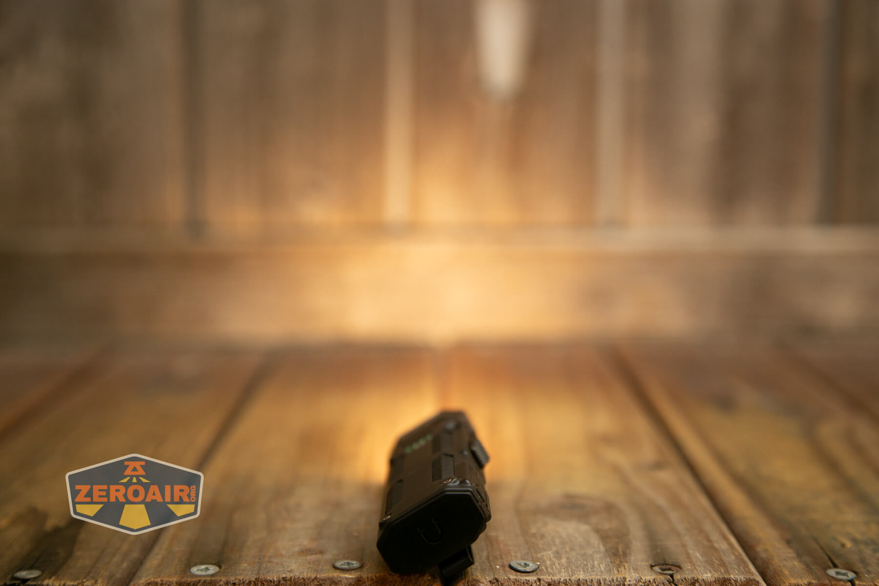 A flashlight shines a warm beam of light onto a wooden surface and wall, with the ZeroAir logo visible in the lower left corner of the image.