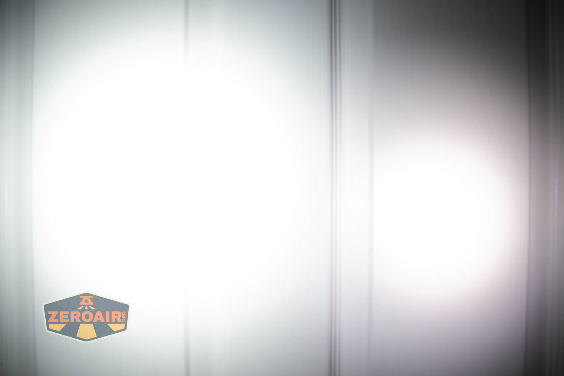 A white vertical-striped surface illuminated by two overlapping circular beams of light, with the ZeroAir logo in the bottom left corner.