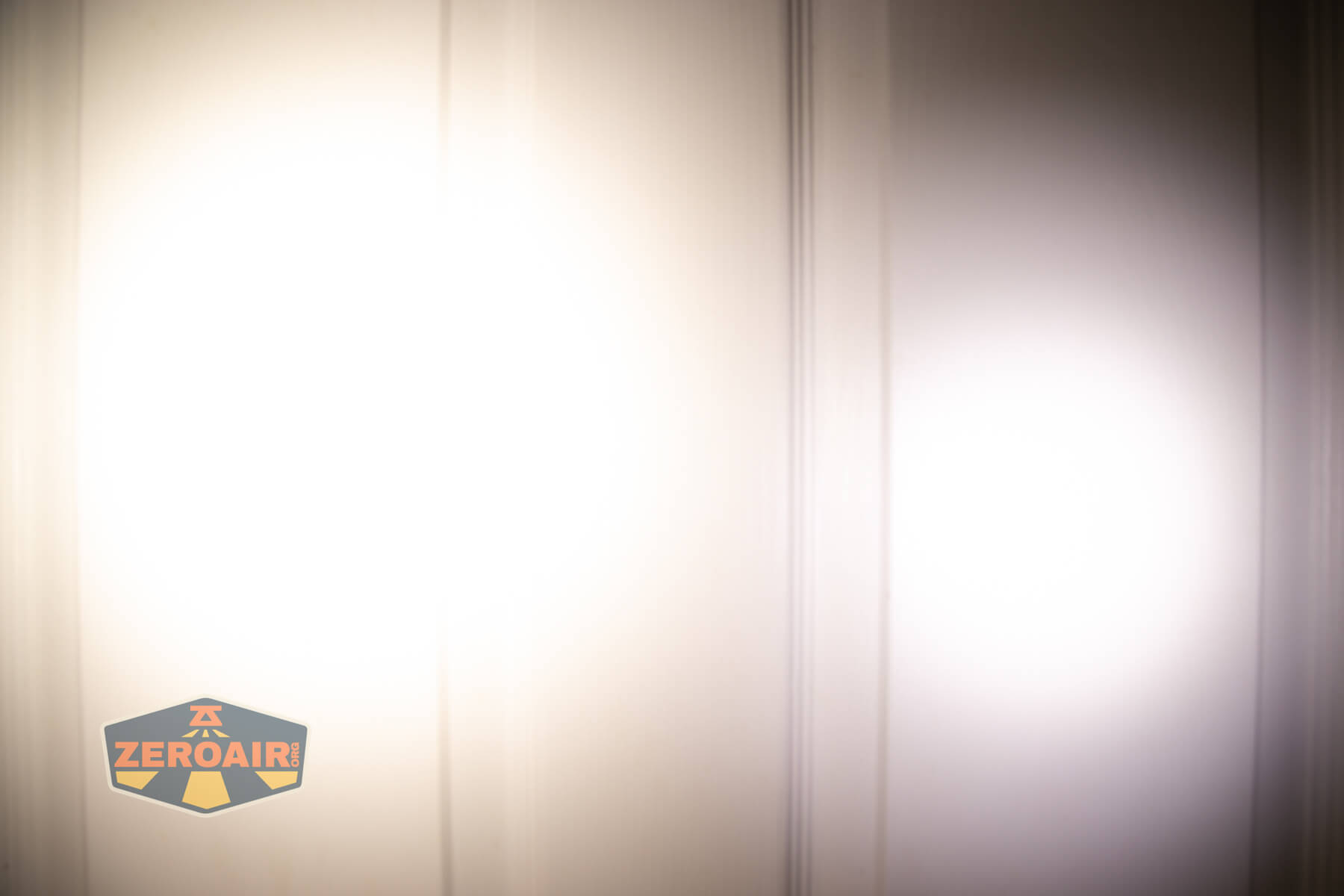 Two distinct circular beams of light are projected onto a light-colored wall with visible vertical lines. A “ZeroAir” logo appears in the lower left corner of the image.