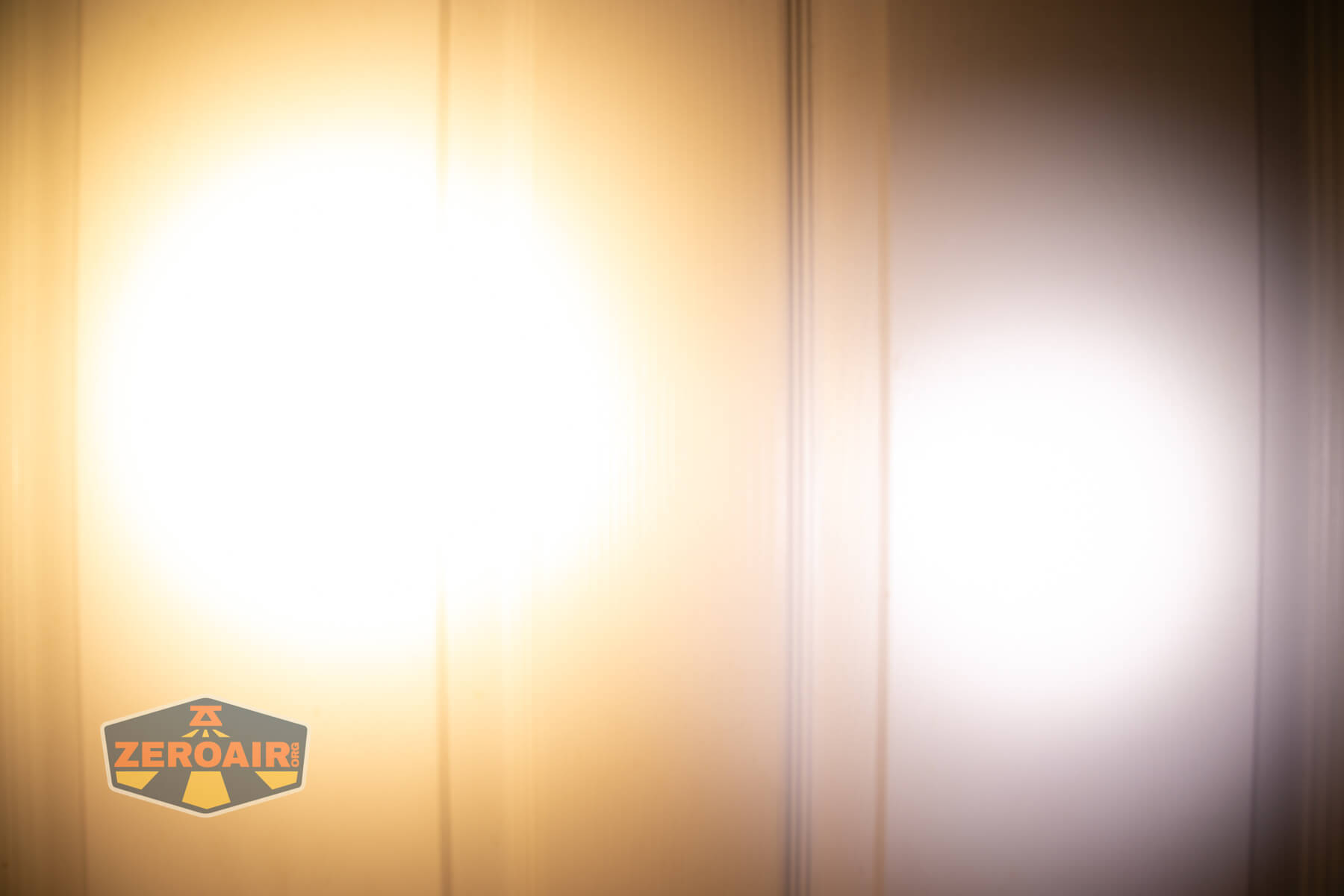 Two overlapping flashlight beams, one warm white on the left and one cool white on the right, are projected onto a wall. The ZeroAir logo appears in the lower left corner of the image.