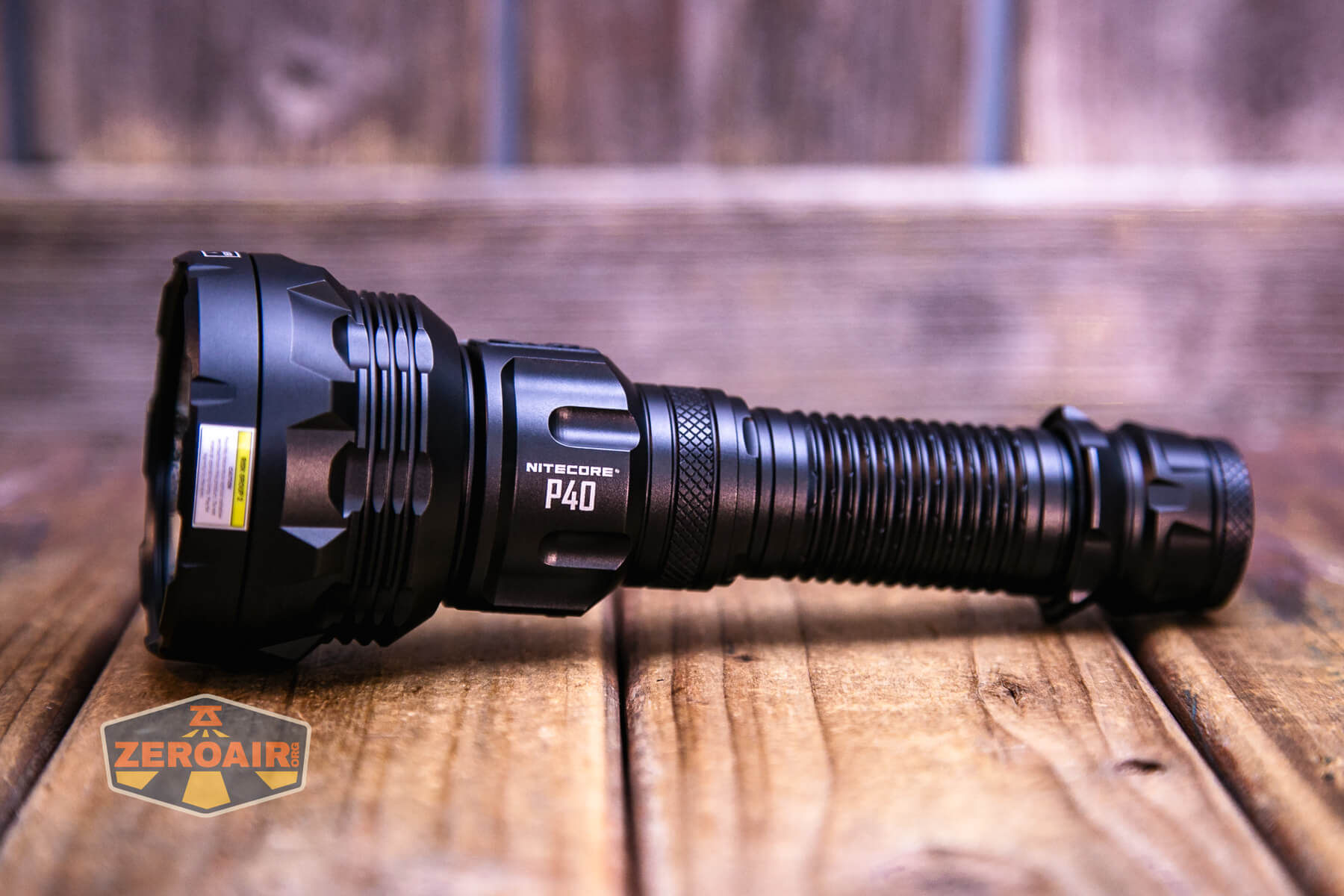 A black Nitecore P40 flashlight is lying on a wooden surface with a blurred wooden background. The ZeroAir logo appears in the lower left corner of the image.