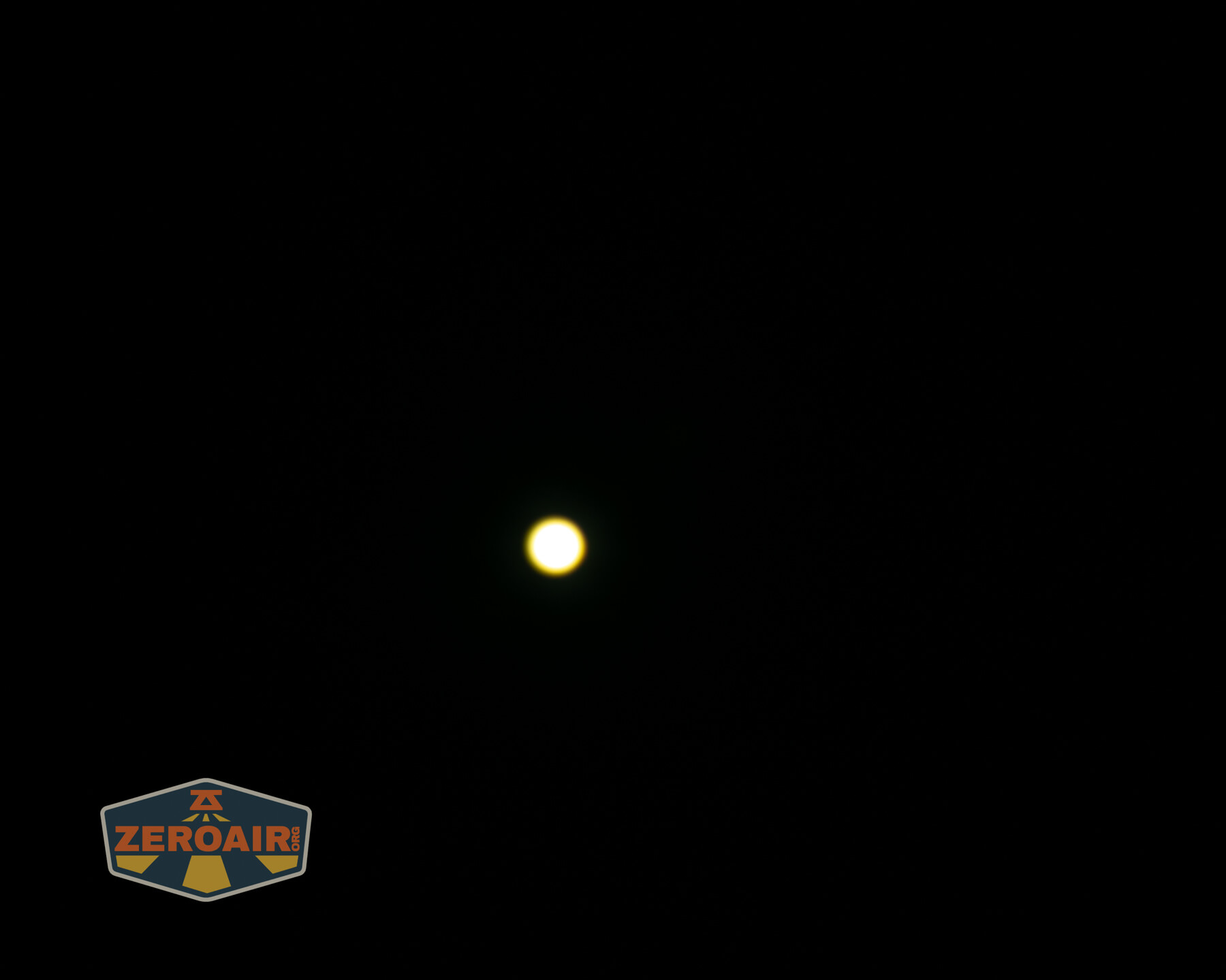 A bright, circular yellow light is centered against a completely black background. A small logo with ZEROAIR text is in the lower-left corner.