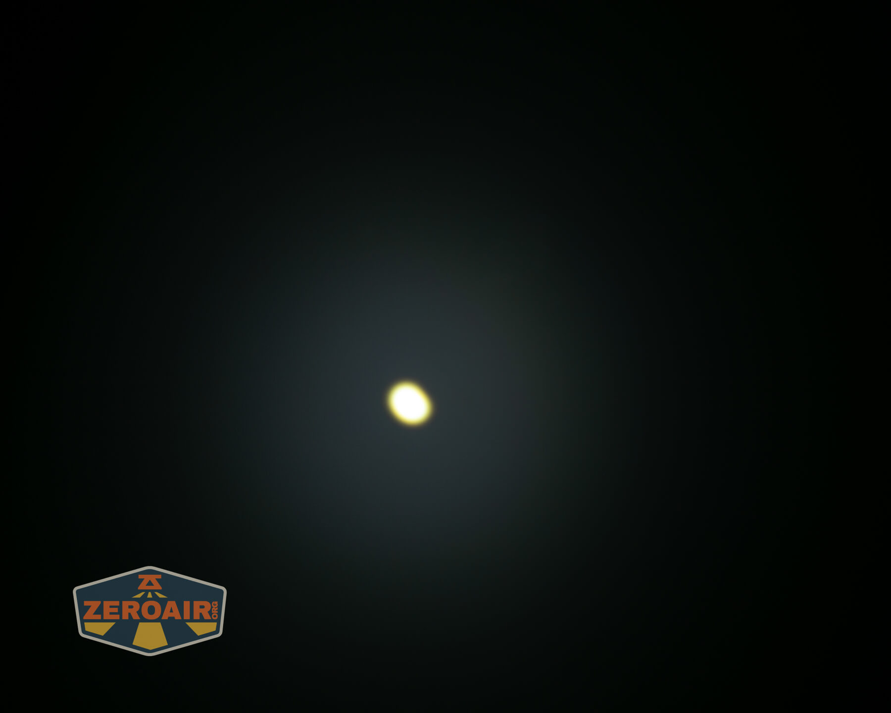 A bright, circular light source appears in the center of a dark background. The image has a faint glow around the light. A logo reading ZEROAIR is in the bottom left corner.