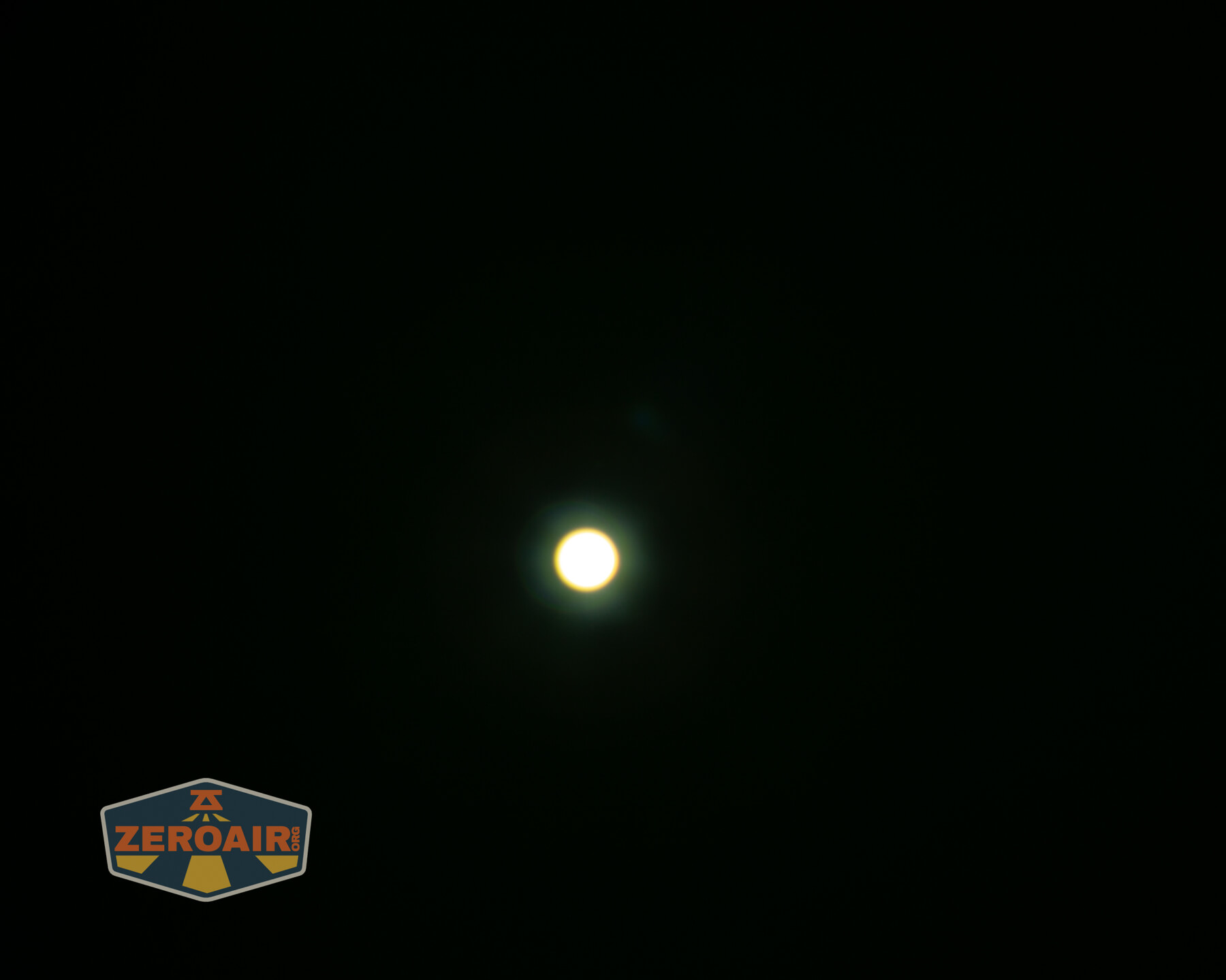 A bright circular light source is centered against a dark background. A faint glow surrounds the light. The ZeroAir logo is present in the bottom left corner.