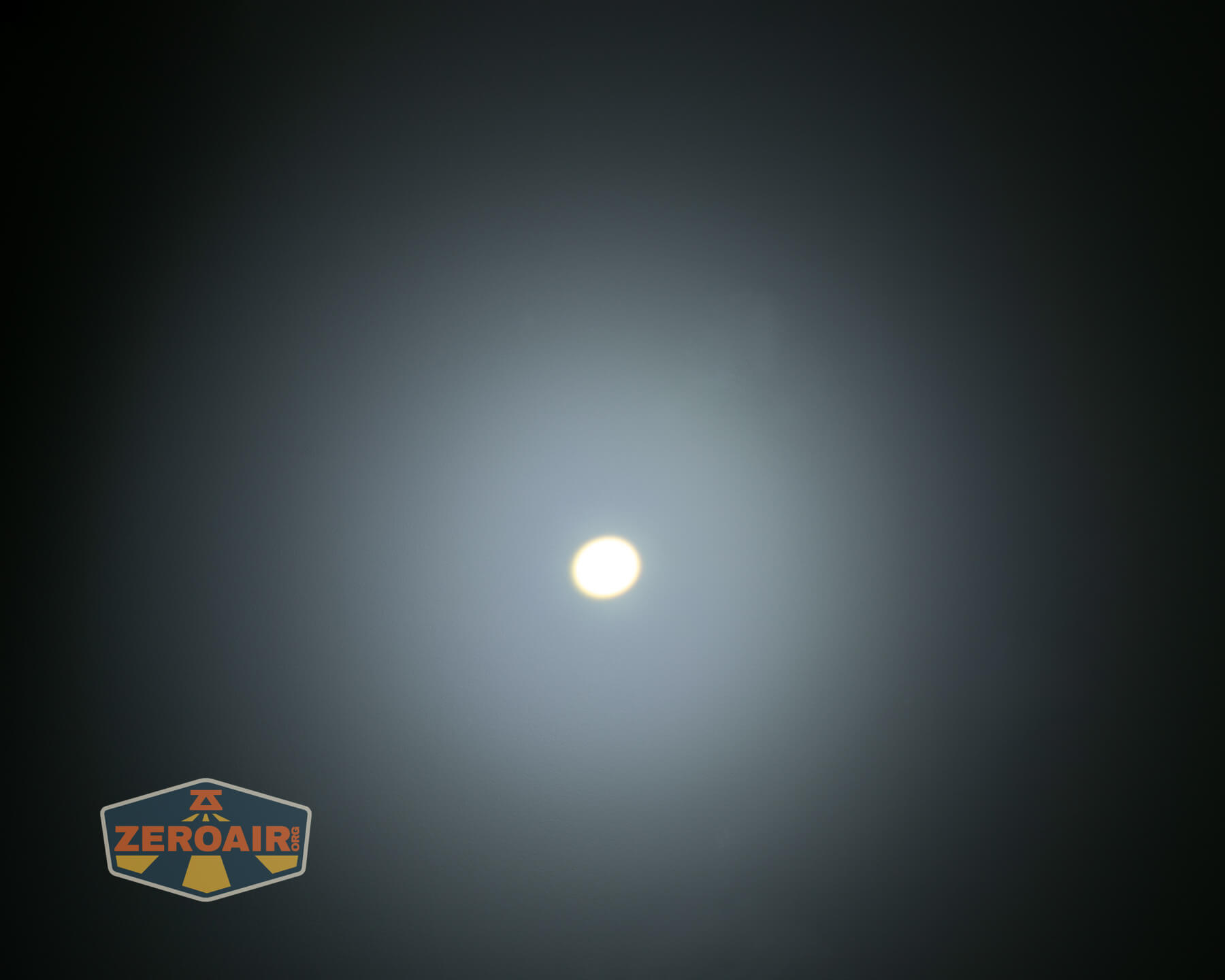 A bright white circular light source in the center of a dark background, creating a glowing halo effect. The ZeroAir logo is in the lower left corner.