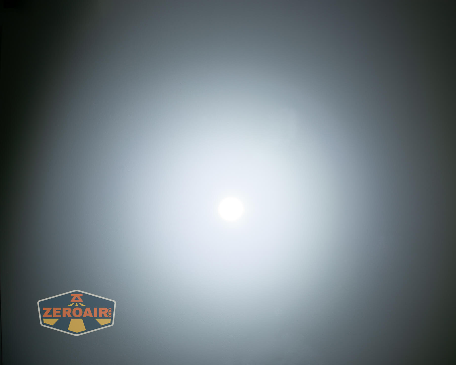 A bright white circle in the center of the image radiates light against a dark gray background. In the lower left corner, there is a logo with the text ZEROAIR inside a shield-shaped design.