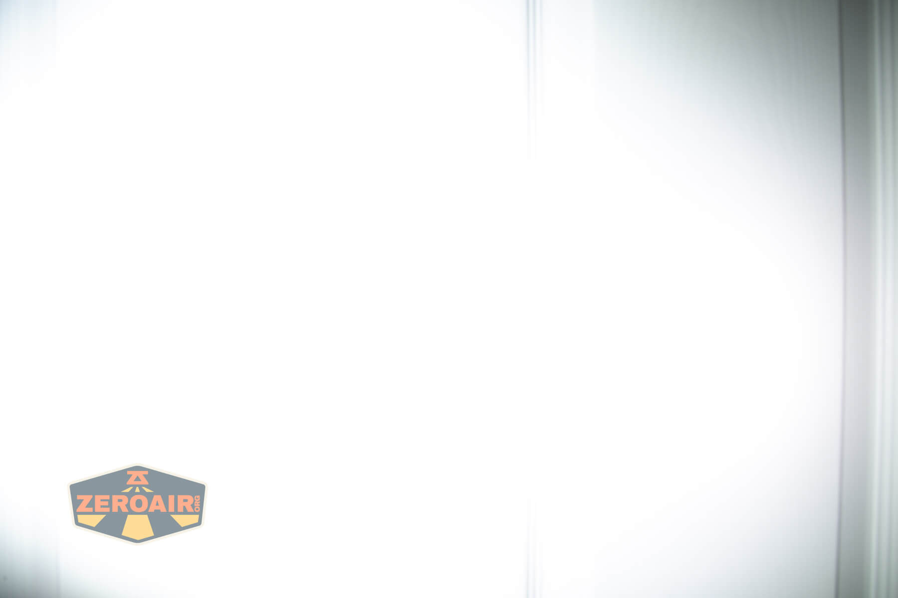 A mostly overexposed white image with faint vertical lines and gradients, featuring a small ZeroAir logo with black, orange, and gray colors in the lower left corner.