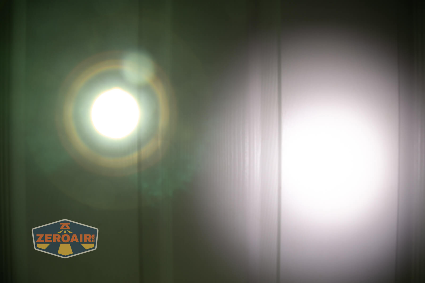 Two bright flashlight beams are projected onto a white wall, creating circular light patterns. The left beam shows visible lens flares and a greenish halo. The ZeroAir logo is in the lower left corner.