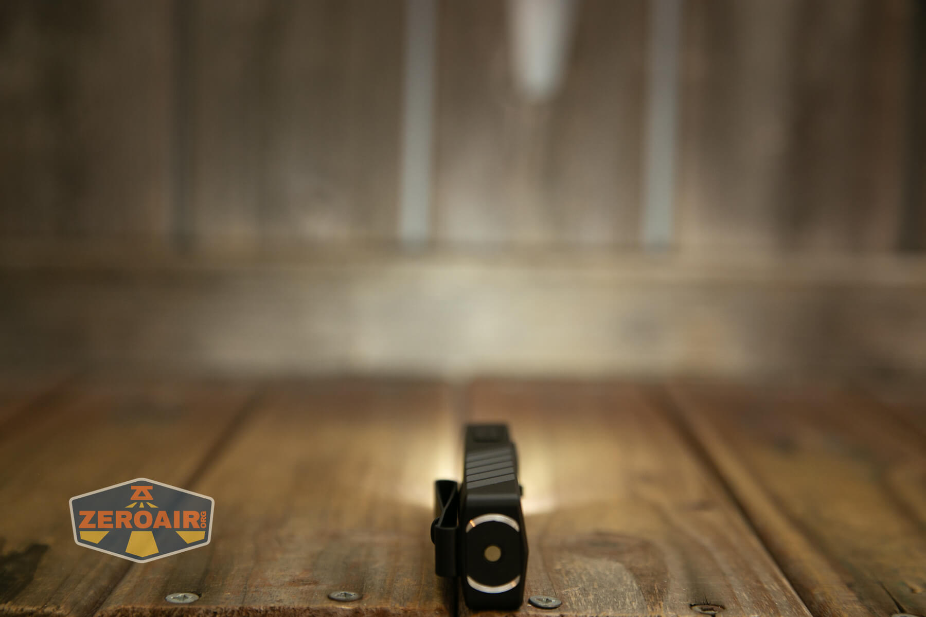 A small black flashlight stands upright on a wooden surface, casting a light on the wood. The background is blurred. The ZeroAir logo appears in the bottom left corner.