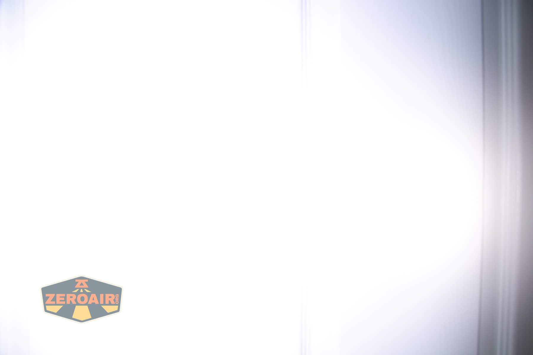 A vertical image with a bright white overexposed center and faded gray edges. A badge-shaped ZEROAIR! logo is in the lower left corner. The image appears washed out with indistinct details.