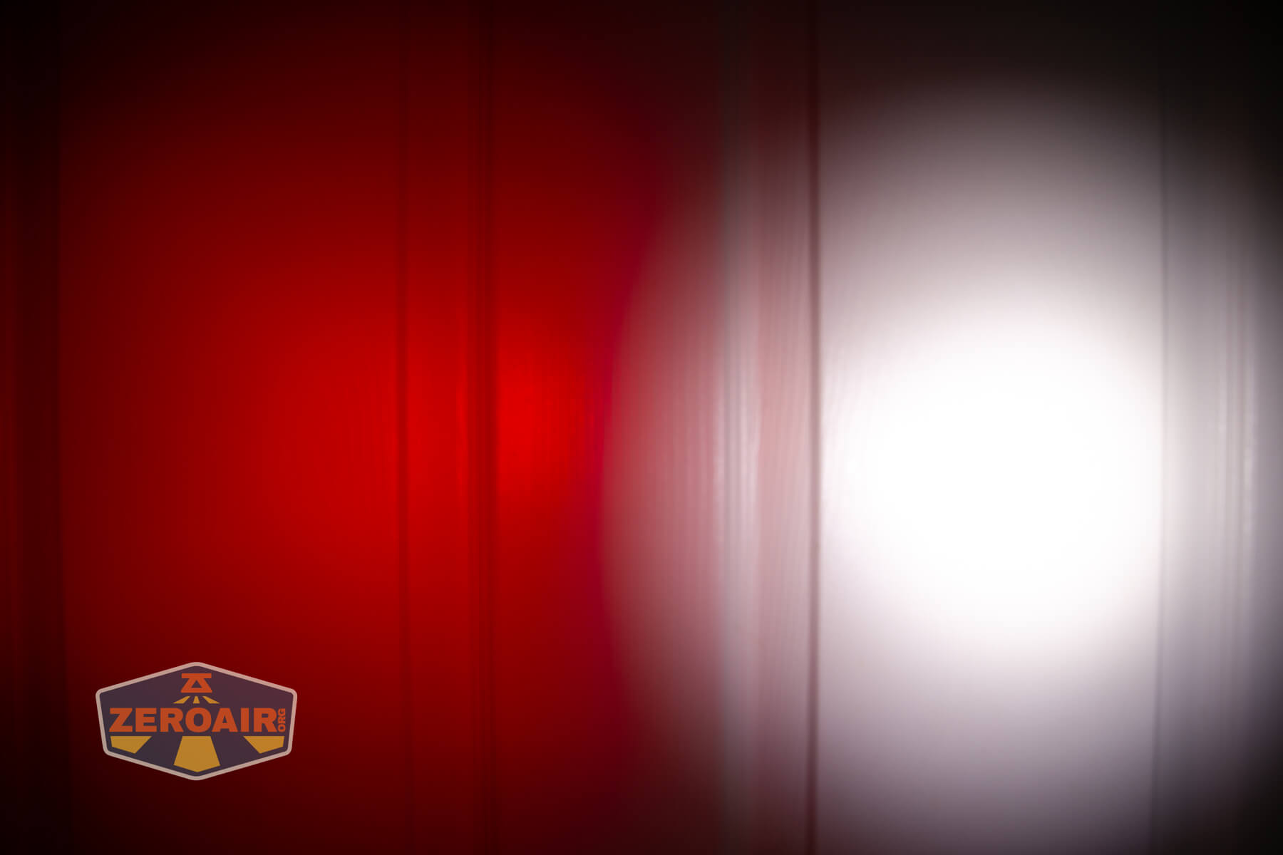 A vertical panel illuminated by two flashlight beams, one red on the left and one white on the right, with the ZeroAir logo in the bottom left corner. The lights create visible gradients and shadows on the surface.