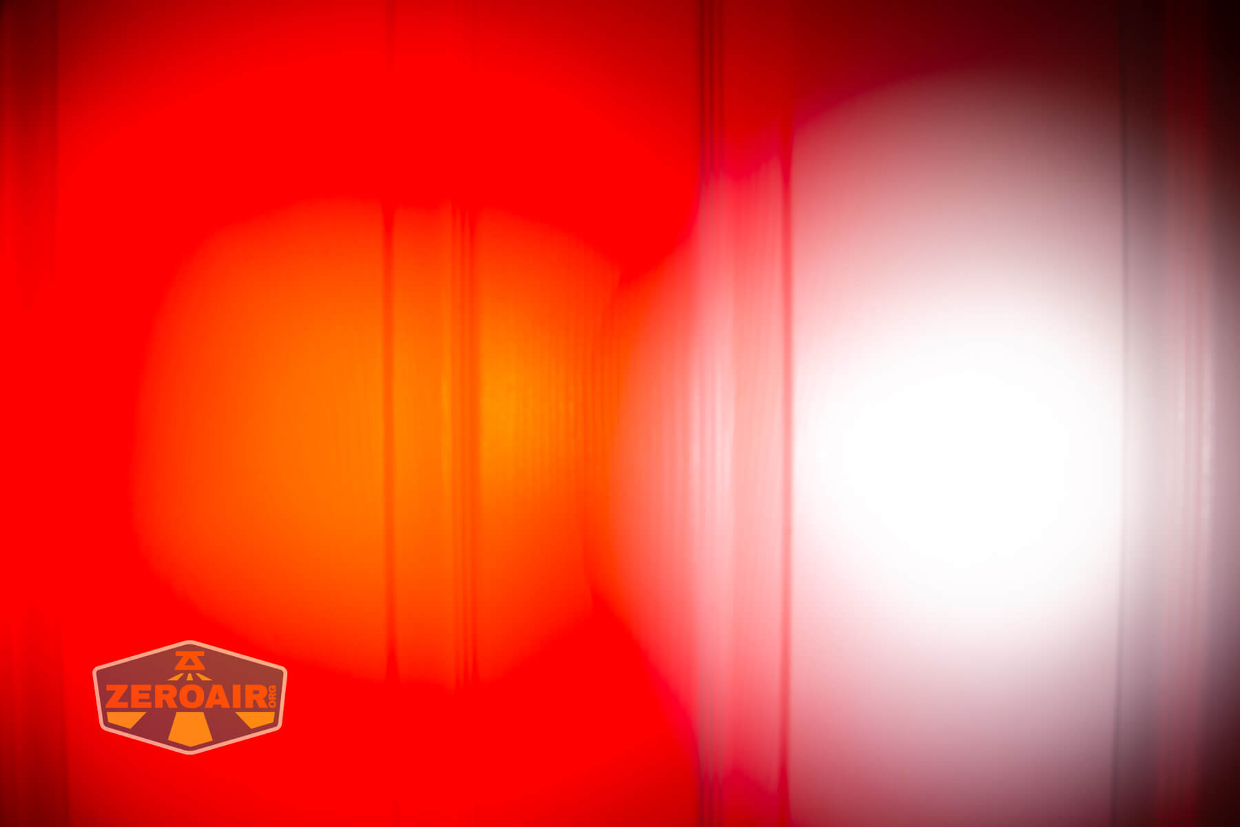 A bright, intense red light and a white light shine side by side on a textured vertical surface. The Zeroair logo is visible in the bottom left corner of the image.