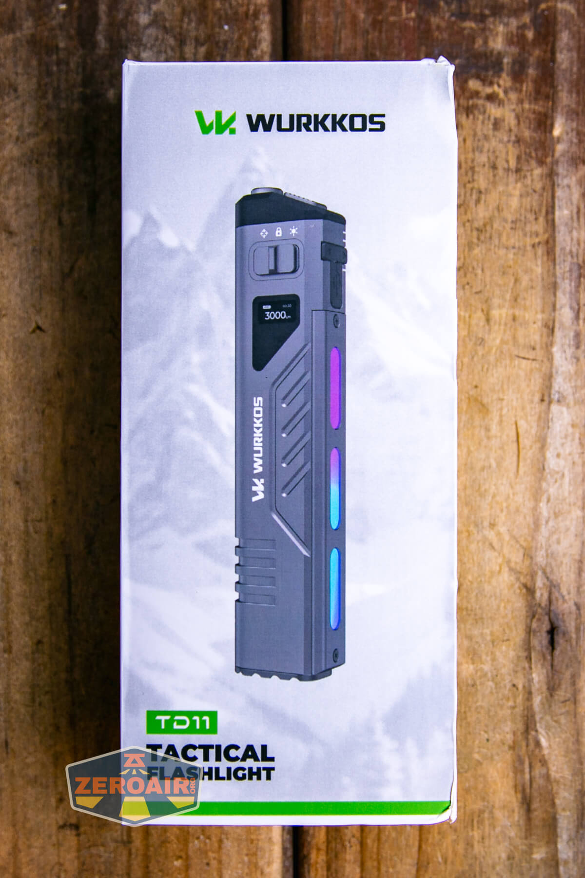 A Wurkkos TD11 tactical flashlight in its packaging, shown standing upright on a wooden surface. The box displays the product image, brand name, and model information.