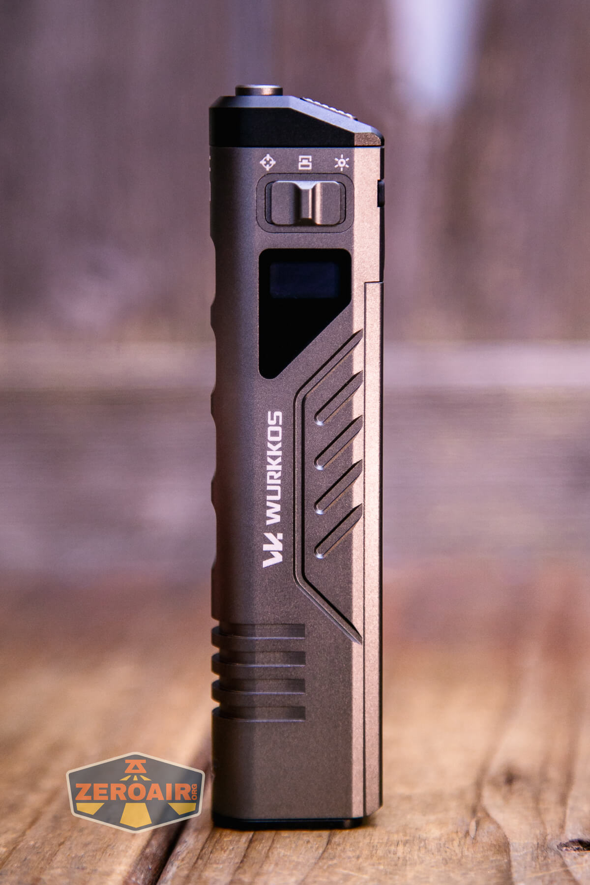 A bronze-colored Wurkkos branded flashlight stands upright on a wooden surface, with a button, indicator icons, and display visible on its body. The ZeroAir logo is in the bottom left corner.