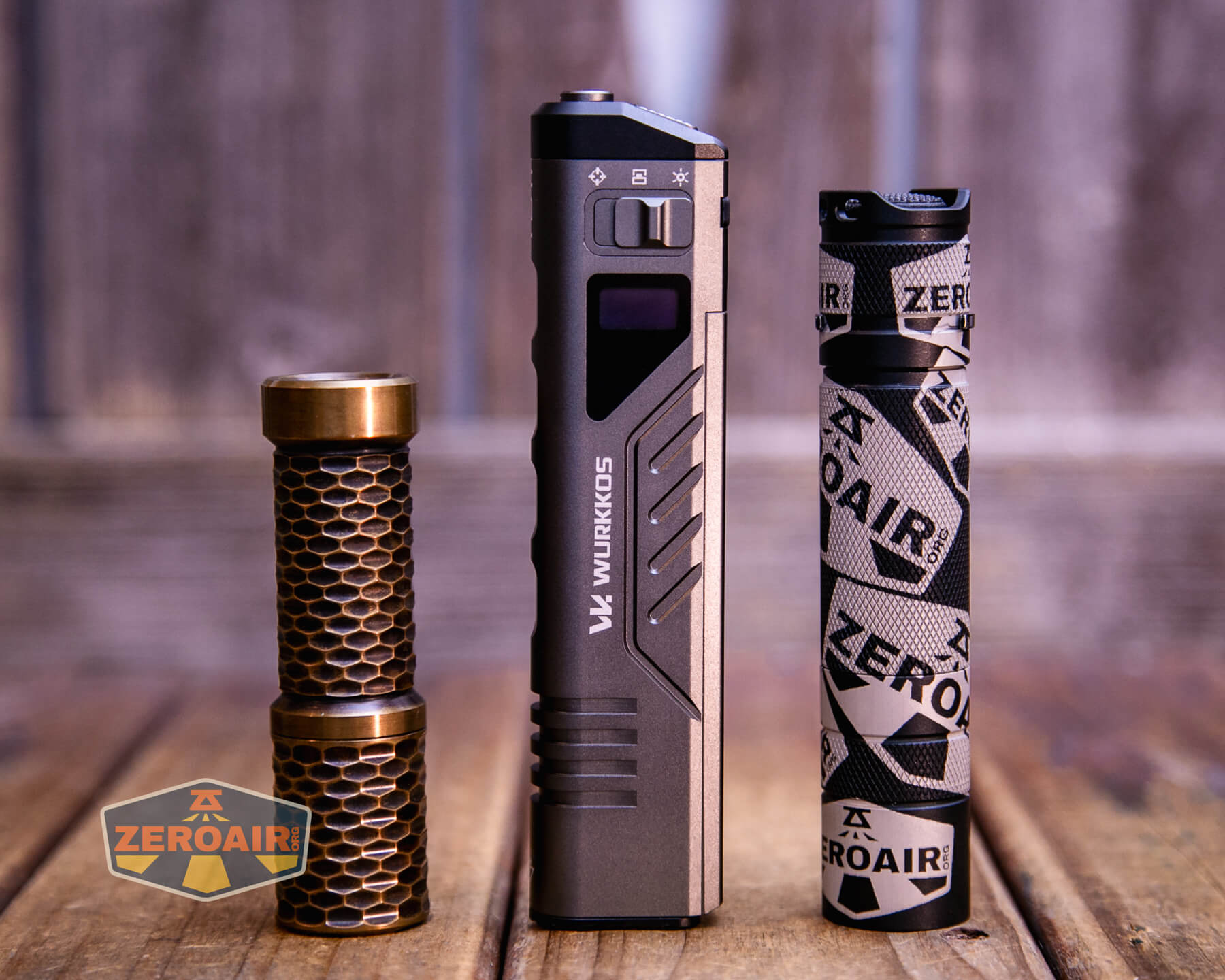 Three cylindrical flashlights are standing upright on a wooden surface. The left flashlight has a honeycomb design, the middle one is larger and rectangular, and the right one is black with branded “ZEROAIR” wrap.