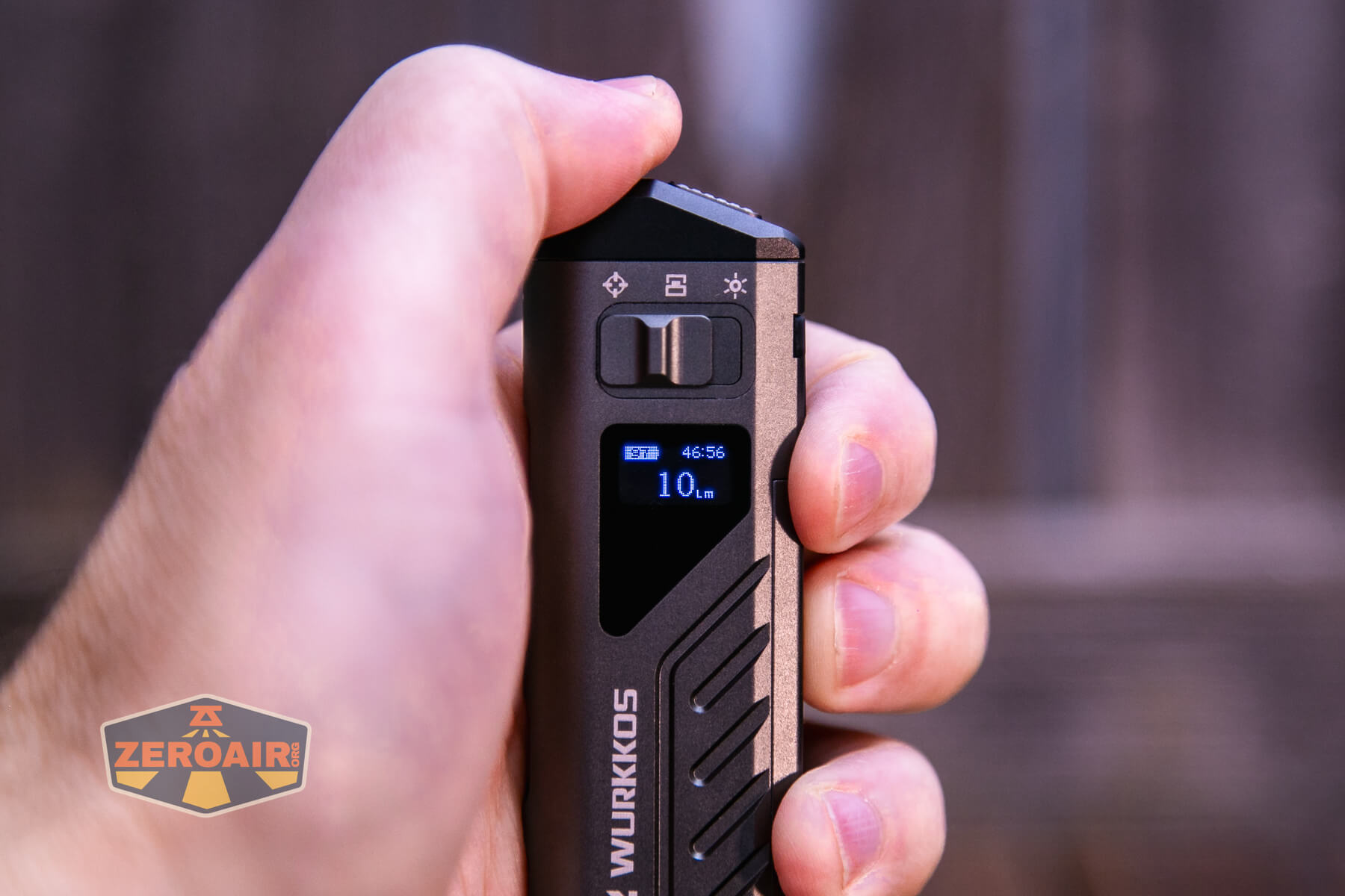 A hand holding a black and metallic Wurkkos device, displaying a small blue screen with the number 10 and some icons. The background is blurred and features the ZeroAir logo in the foreground.