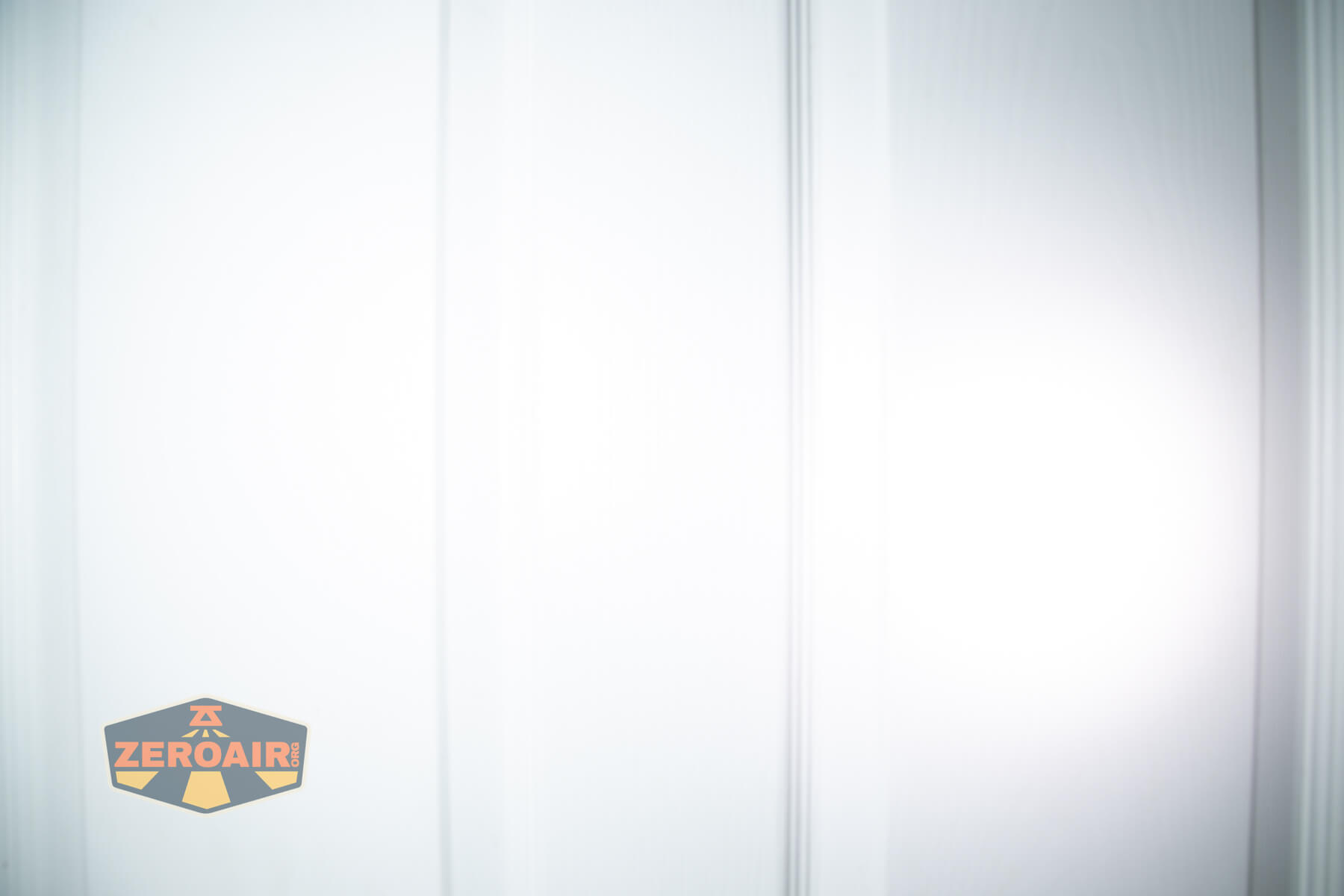 Close-up of a white paneled door with bright light shining on the right side. A small logo reading ZEROAIR is visible in the lower left corner.