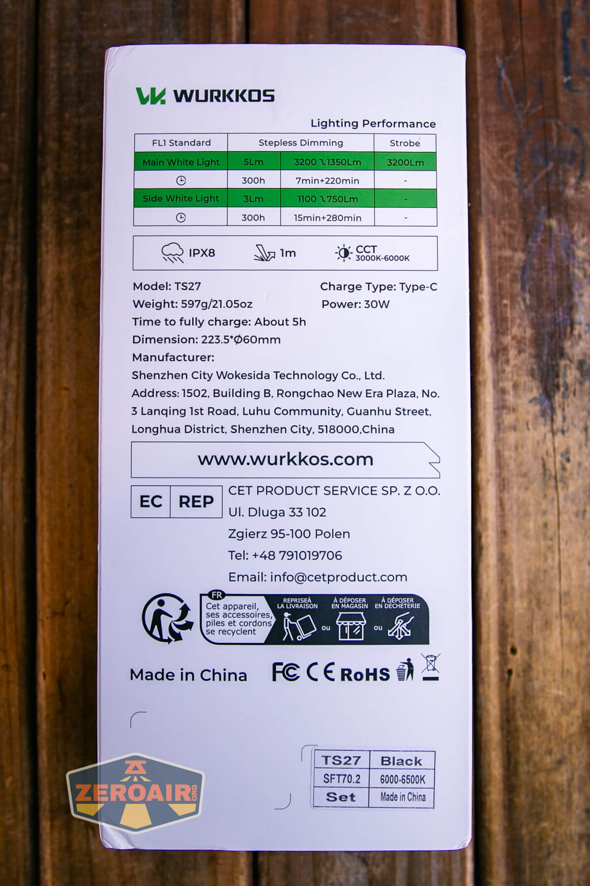 The back of a Wurkkos flashlight box showing technical specifications, lighting performance details, manufacturer information, certification icons, and a Zeroair sticker on a wooden surface.