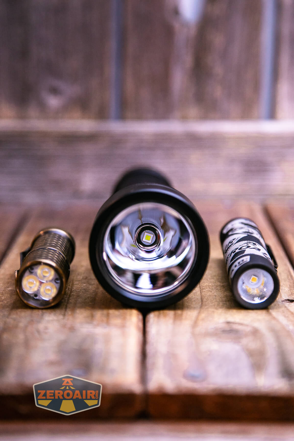 A close-up of three flashlight components on a wooden surface: a bare LED module, a flashlight reflector with LED, and a cylindrical battery, with a ZeroAir logo in the corner.