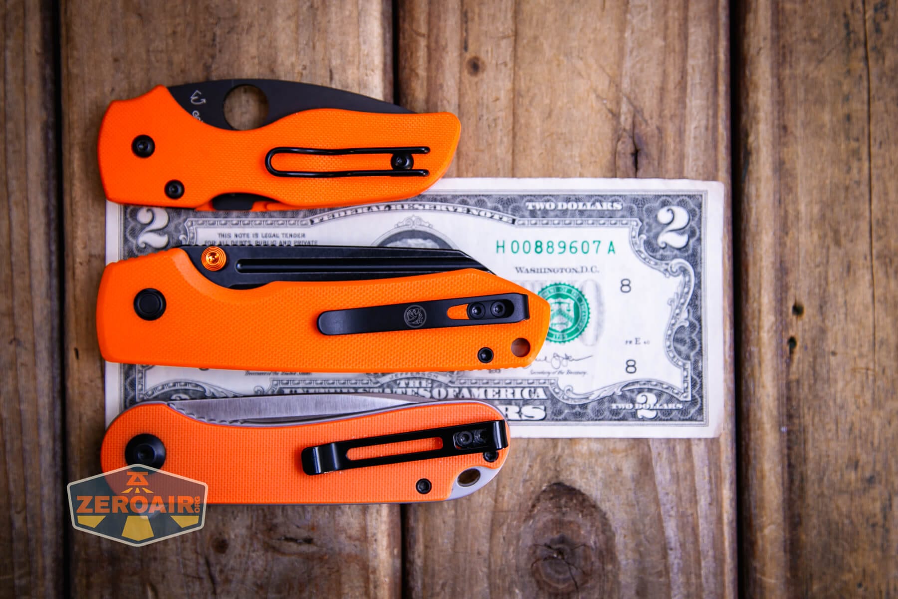 Vosteed Raccoon TLL Orange G10 knife on a two dollar bill compared to Civivi Elementum in orange
