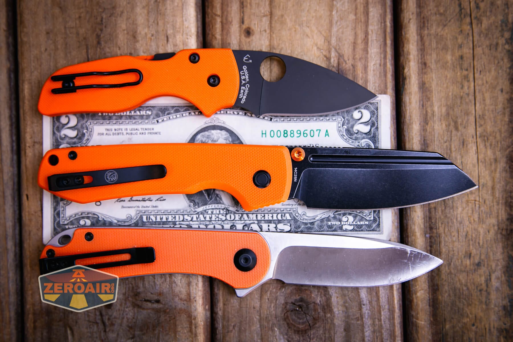 Vosteed Raccoon TLL Orange G10 knife on a two dollar bill compared to Civivi Elementum in orange