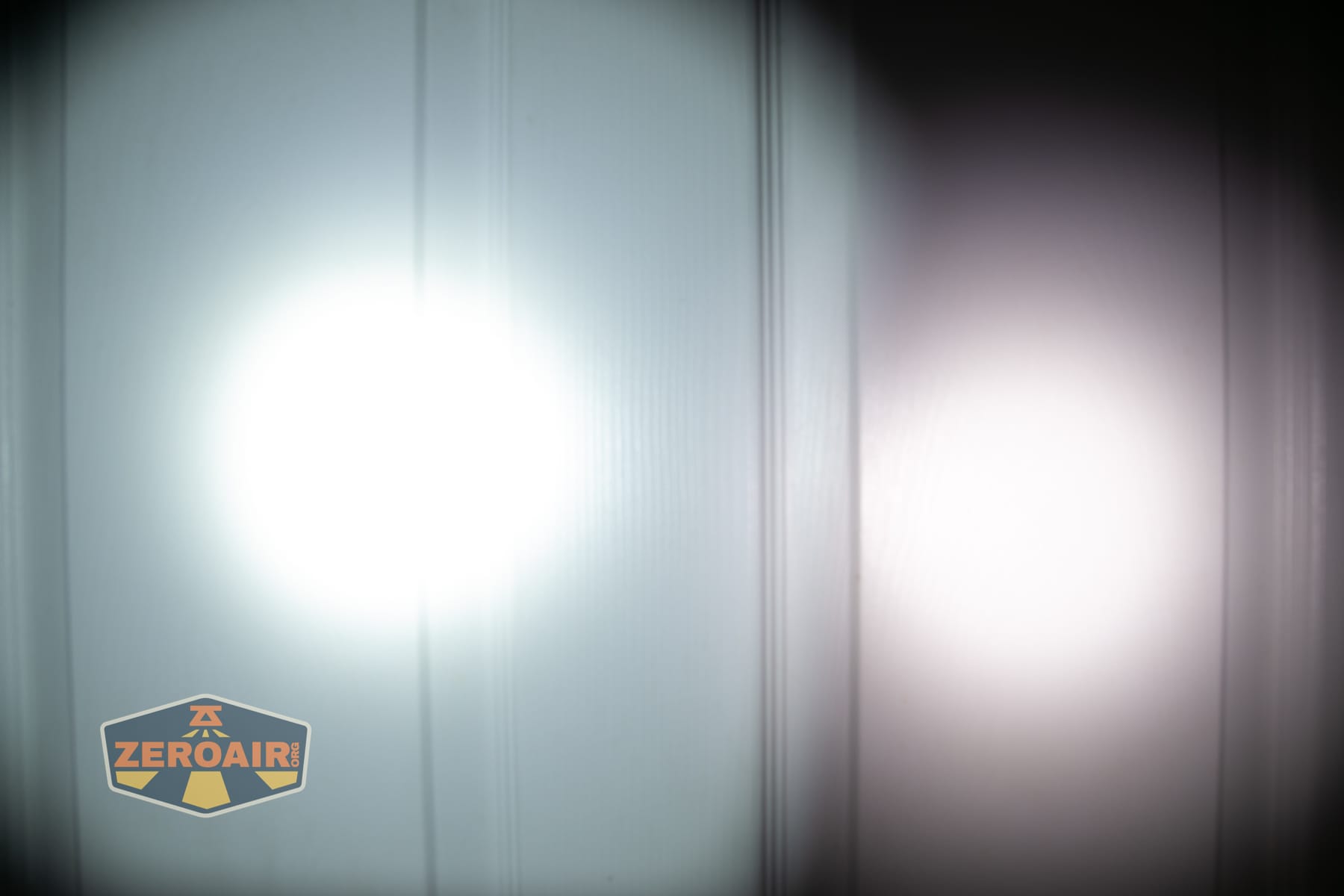 Olight Arkpro Stars and Stripes flat flashlight beamshots on door compared to Nichia 219b