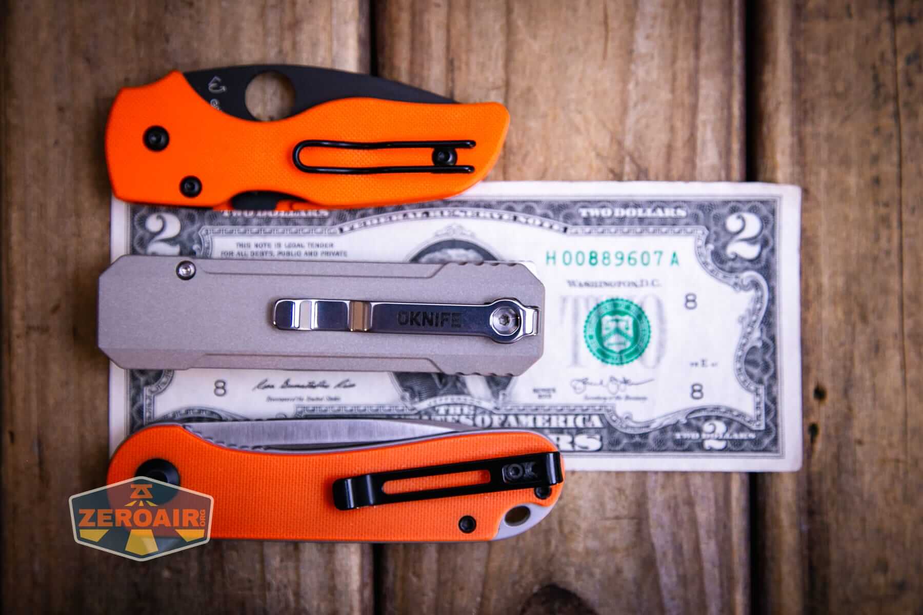 Olight Oknife LK folding knife flashlight on a two dollar bill compared to Civivi Elementum in orange
