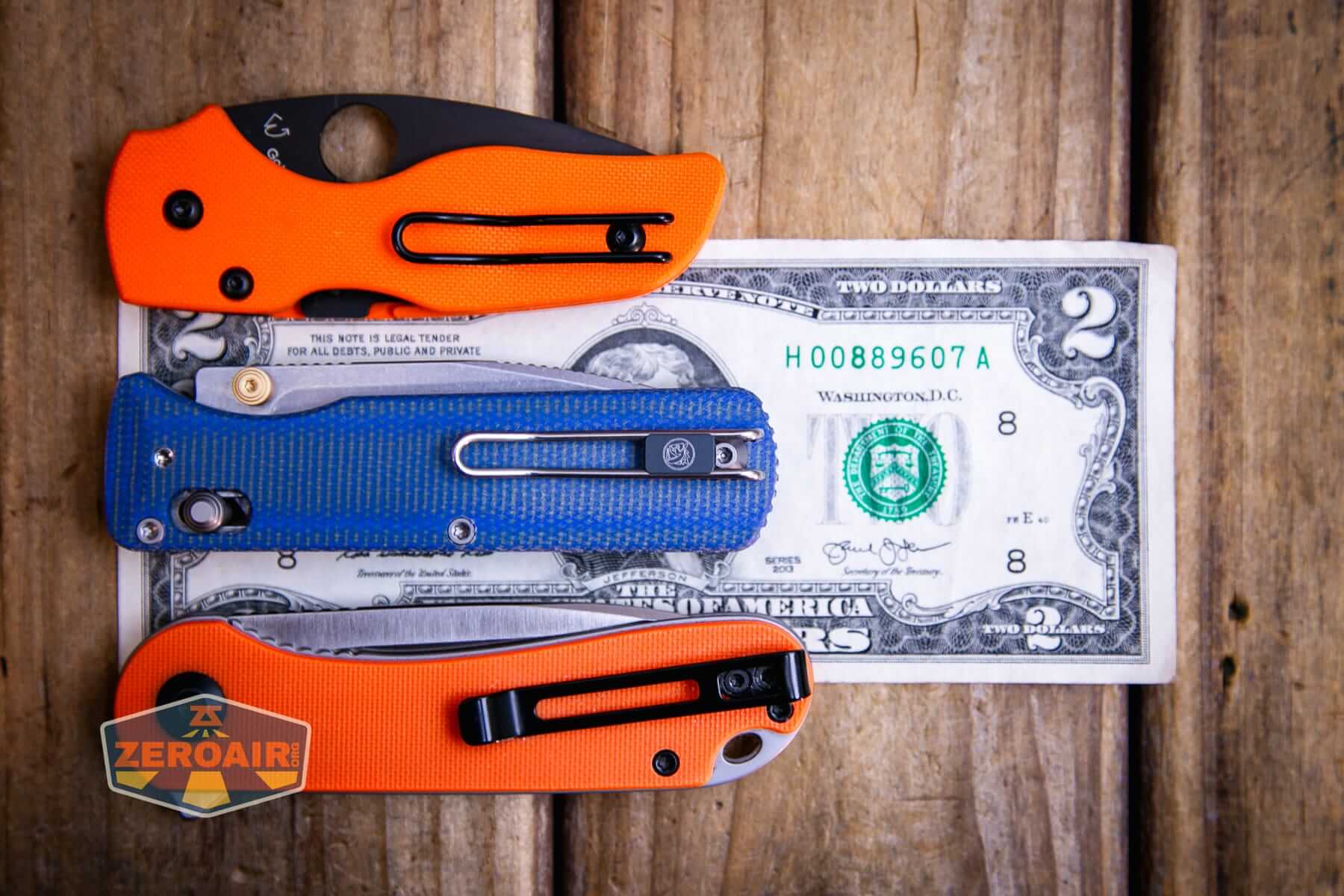 Vosteed Vombat Modswap knife on a two dollar bill compared to Civivi Elementum in orange